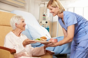 Nurse Serving Meal To Senior Female Patient Sitting In Chair
